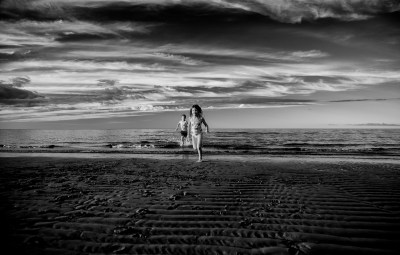 brother and sister running on the beach with a beautiful sunset sky